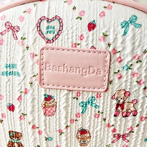 Détail du tissu fleuri matelassé avec étiquette de marque en cuir rose sur sac à dos