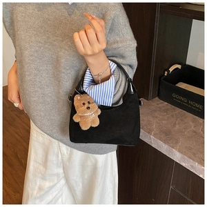 Detail of black suede crescent bag with a plush bear charm and glossy top handle