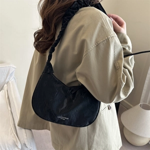 Sac à bandoulière noir minimaliste avec sangle nuage porté sur un trench-coat beige