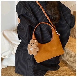 Detail of a brown suede half-moon shoulder bag with chain and plush bear charm accessory