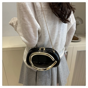 Detail of minimalist black patent leather shoulder bag with large gold sculptural hardware