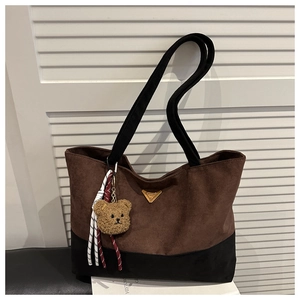 Detalle de bolso tote de ante marrón con placa dorada y colgante de osito suave