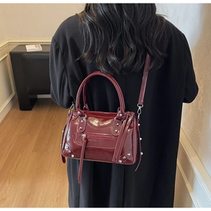Dettaglio borsa da moto bordeaux in pelle verniciata con borchie indossata su cappotto nero