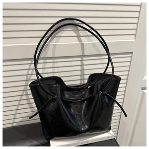 Close-up of black glossy leather tote bag featuring drawstring knot details and sleek texture