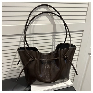 Detailed view of dark brown glossy leather tote bag with drawstring texture and knotted straps