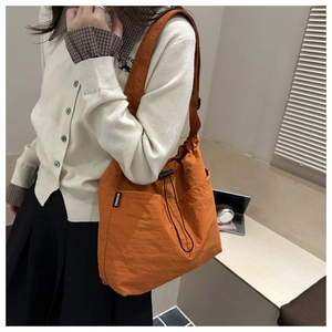 Detailed side view of bright orange waterproof nylon shoulder bag with drawstring closure