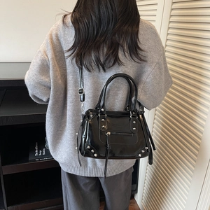 Elegante borsa a tracolla in vernice nera con borchie e nappe indossata da una modella