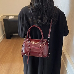 Borsa da moto in pelle verniciata rosso scuro con borchie e nappe su cappotto nero