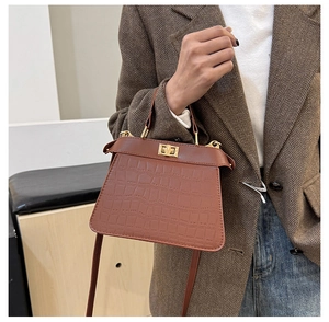 Detail einer braunen Handtasche mit Krokostruktur und goldenem Drehverschluss am Tragegurt