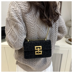 Detail of black leopard print crossbody bag with gold chain and metal lock on grey sweater