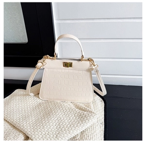 Makro-Detail der cremeweissen Handtasche mit Krokodil-Prägung und goldenem Drehverschluss