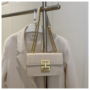 Detail of cream leopard textured leather bag with gold chain strap on a white blazer