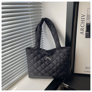 Close-up of black quilted tote bag with silver metal bow and rhombic texture details
