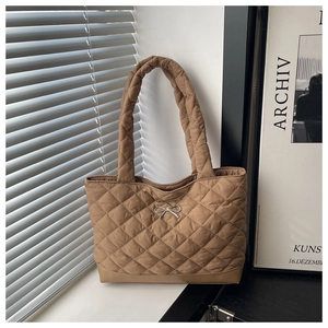 Detail of a brown quilted tote bag featuring a small silver bow and a padded shoulder strap