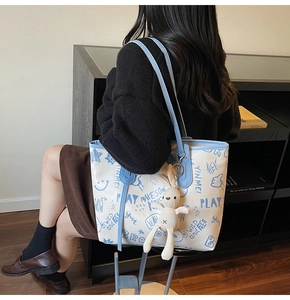 Detail view of large white tote bag with blue graffiti, rabbit charm and shoulder strap