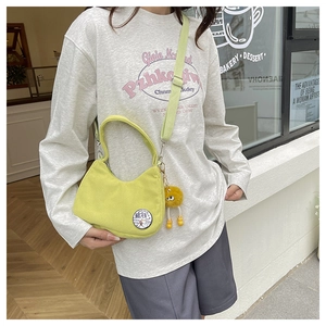 Détail du sac bandoulière en velours côtelé vert citron avec écusson et breloque peluche jaune