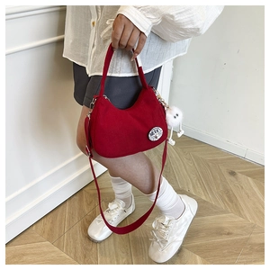Détail du sac bandoulière bordeaux en velours côtelé avec badge et peluche blanche