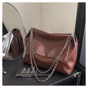 Détail de la texture en cuir ciré marron foncé et de la chaîne argentée du sac chic