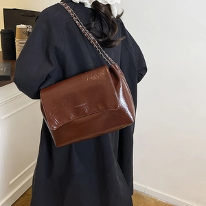 Sac bandoulière marron moderne en similicuir brillant porté par un mannequin en extérieur