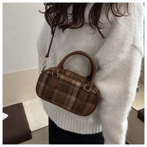 Detailed view of plaid wool bag with dark brown leather handles and gold hardware