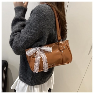 Detail of a brown glossy underarm bag featuring a large white lace bow on the side