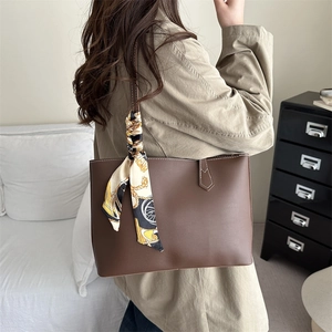 Brown faux leather tote bag with contrast stitching and decorative scarf on the handle