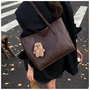 Detail of deep brown faux leather tote bag with plush bear charm in autumn street setting