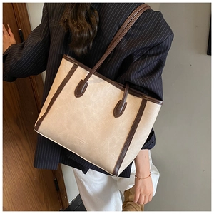 Close-up of a large beige tote bag with brown trim held by a model in a blazer