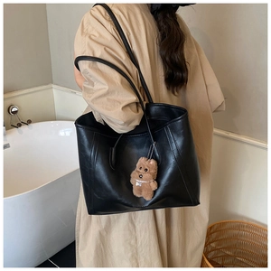 Gros plan du sac fourre-tout en cuir noir avec un charm ours en peluche brun sur la bandoulière
