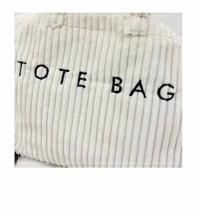 Detail shot of beige corduroy tote bag showing ribbed texture and black TOTE BAG embroidery