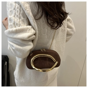 Dettaglio borsa scamosciata marrone con manico in oro e catena su maglione bianco