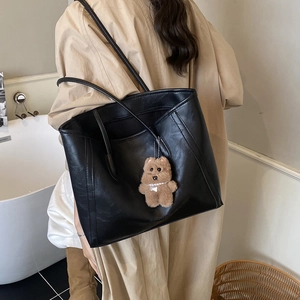 Grand sac cabas noir avec pendentif ours porté à l'épaule par un mannequin en trench beige