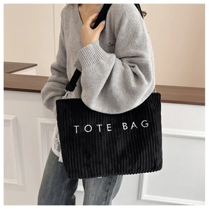 Model wearing a black corduroy tote bag with TOTE BAG embroidery and wide shoulder strap
