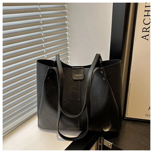 Detail of a black leather tote bag with gold Fashion text and stylish shoulder straps