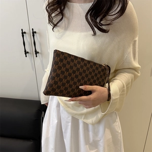Brown monogram printed crossbody handbag with gold zipper shown by model in lifestyle setting