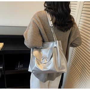 Detail of silver metallic tote bag featuring a decorative metal bow and chain shoulder strap
