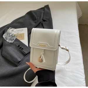 Close-up of white leather crossbody phone bag with gold FASHION lettering and metal charm