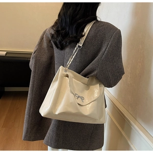 Close-up of cream tote bag featuring a metallic bow detail and leather chain strap