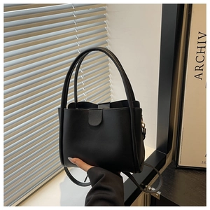 Detail of a black faux leather bucket bag showing dual handles and adjustable shoulder strap