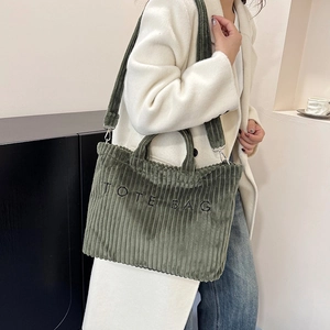 Dark green corduroy tote bag with TOTE BAG embroidery shown on a shoulder
