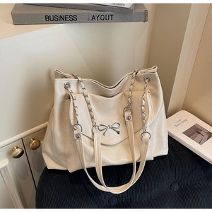 Detail of cream tote bag with metal bow accent and chain shoulder strap on corduroy