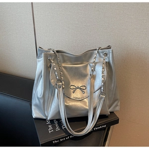 Detail of silver metallic tote bag with decorative metal bow and chain shoulder strap