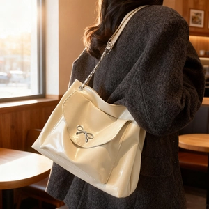 Minimalist cream glossy shoulder bag with silver bow accent and chain strap worn by model