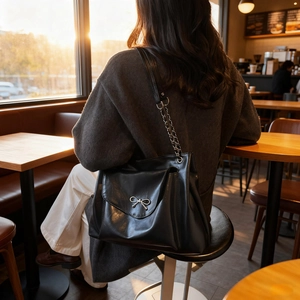 Minimalist black tote bag with silver bow detail shown in a cozy cafe setting
