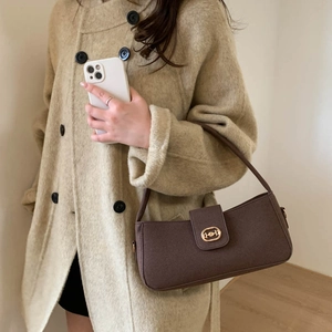 Coffee brown textured crossbody handbag with golden oval buckle worn with beige coat