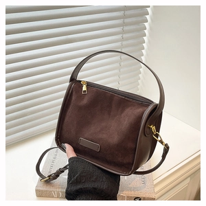 Detail of dark brown suede handbag featuring golden metal hardware and a textured surface