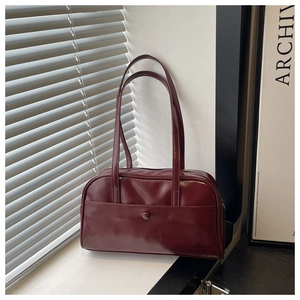 Close-up of a burgundy leather pillow bag with minimalist stitching on a window sill