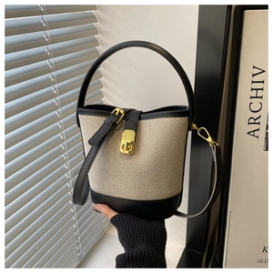 Detail of canvas bucket bag with black leather trim and elegant golden lock closure