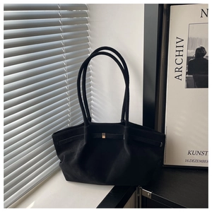 Detail of matte black tote bag with long handles and golden buckle near a window