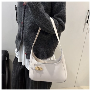 Close-up of a white minimalist underarm bag with gold metal clasp on a model shoulder